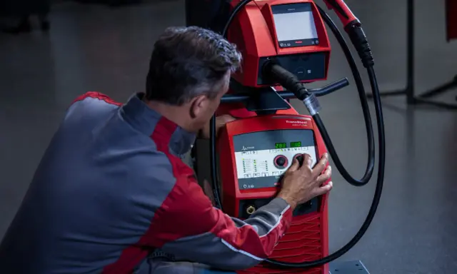 Operatore regola i parametri di saldatura su una macchina Fronius, ottimizzando l'apporto termico per un lavoro preciso.