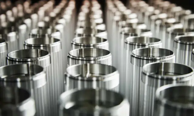 Fila di componenti cilindrici in leghe di alluminio, pronti per la produzione.