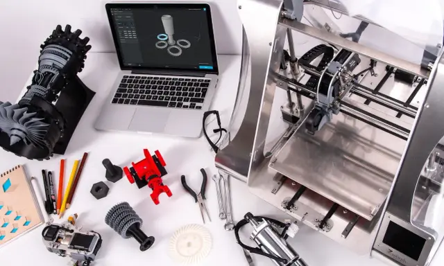 Un programmatore CNC progetta e stampa componenti complessi. Laptop con modello 3D, stampante 3D, parti meccaniche e attrezzi.