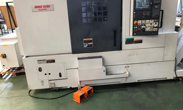 Tornio Mori Seiki NL2500 in officina, con pannello di controllo e pedali arancioni.
