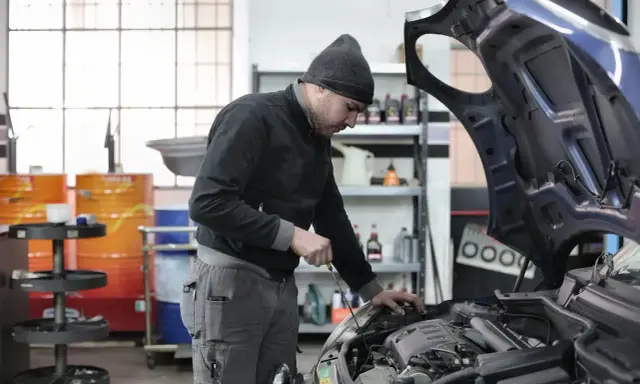 Giovane apprendista meccanico al lavoro, mentre controlla il motore di un'auto. Chissà quanto guadagna un apprendista meccanico con questa dedizione.