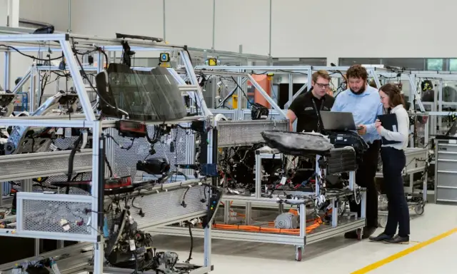 Operai di produzione analizzano schemi su un laptop, lavorando su un telaio di assemblaggio di un veicolo.