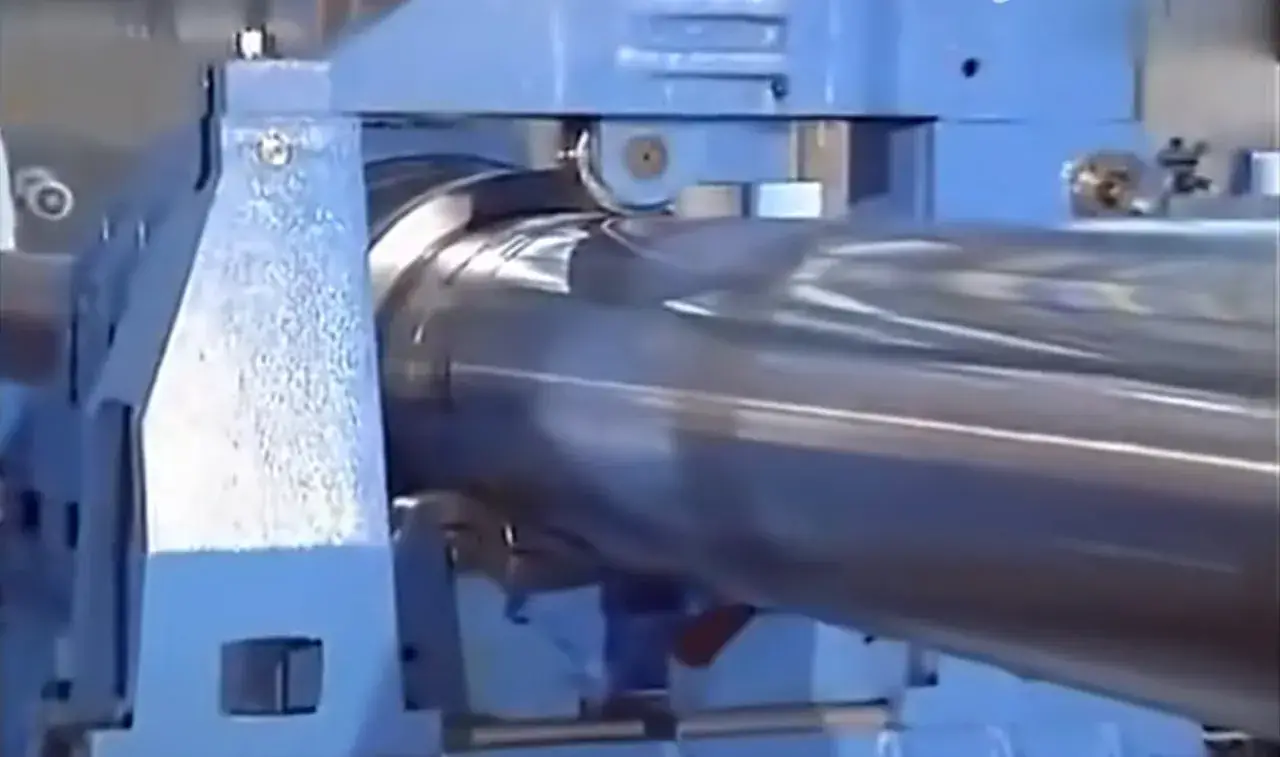 Macchinario industriale blu in azione, impegnato in una **foratura profonda** su un grande cilindro metallico lucido.