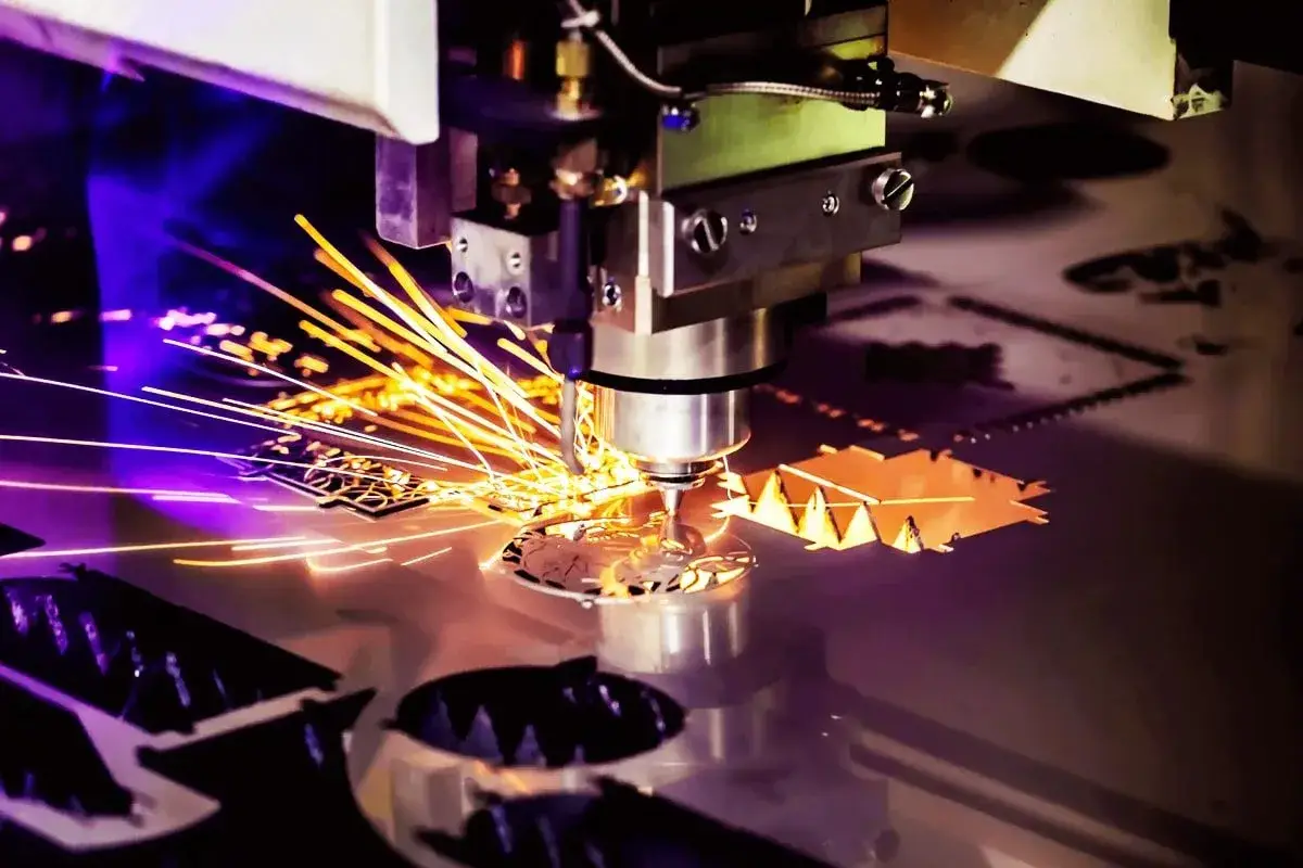 Macchina per **taglio laser** in azione, con scintille dorate che volano mentre crea forme precise su un foglio di metallo.
