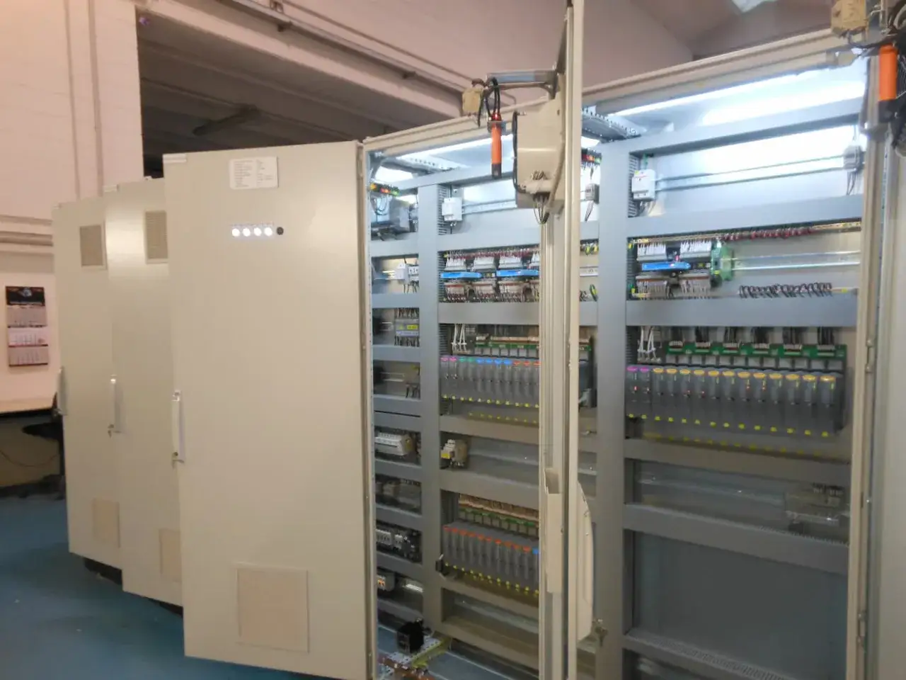 Armadio elettrico aperto con numerosi componenti PLC colorati e cablaggi ordinati.
