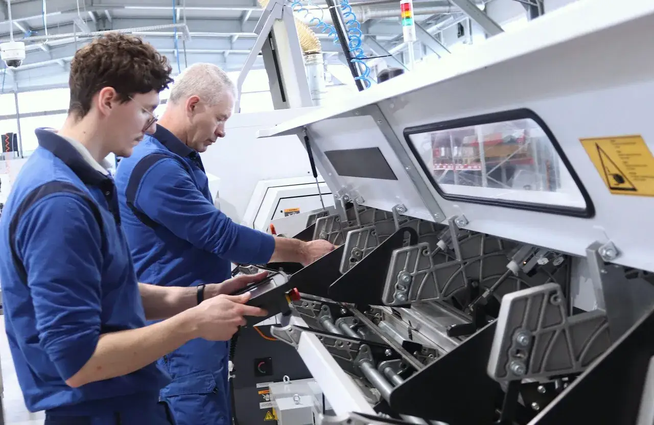 Un programmatore CAD CAM lavora su una macchina industriale, con un collega che controlla un tablet.