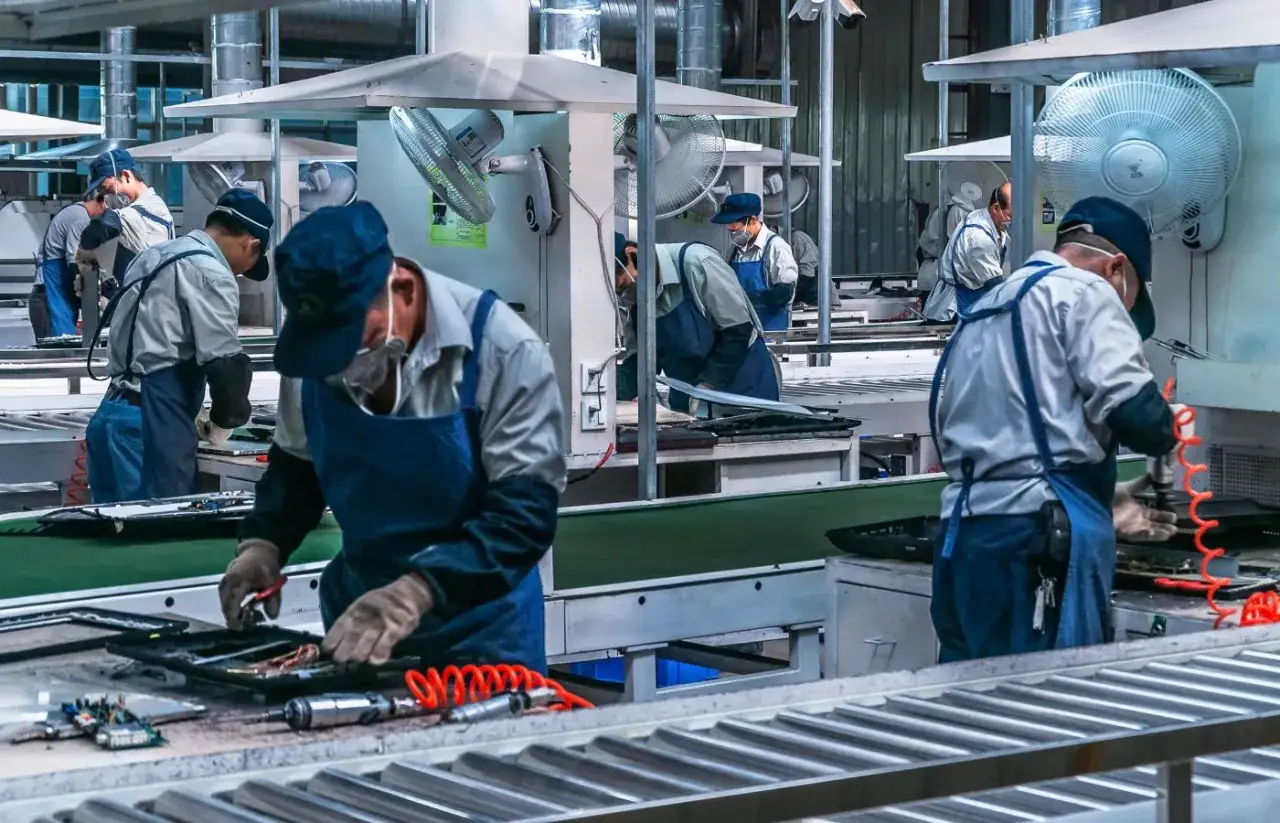 Operaio di produzione assembla componenti elettronici su una linea di montaggio, concentrato sul suo lavoro.