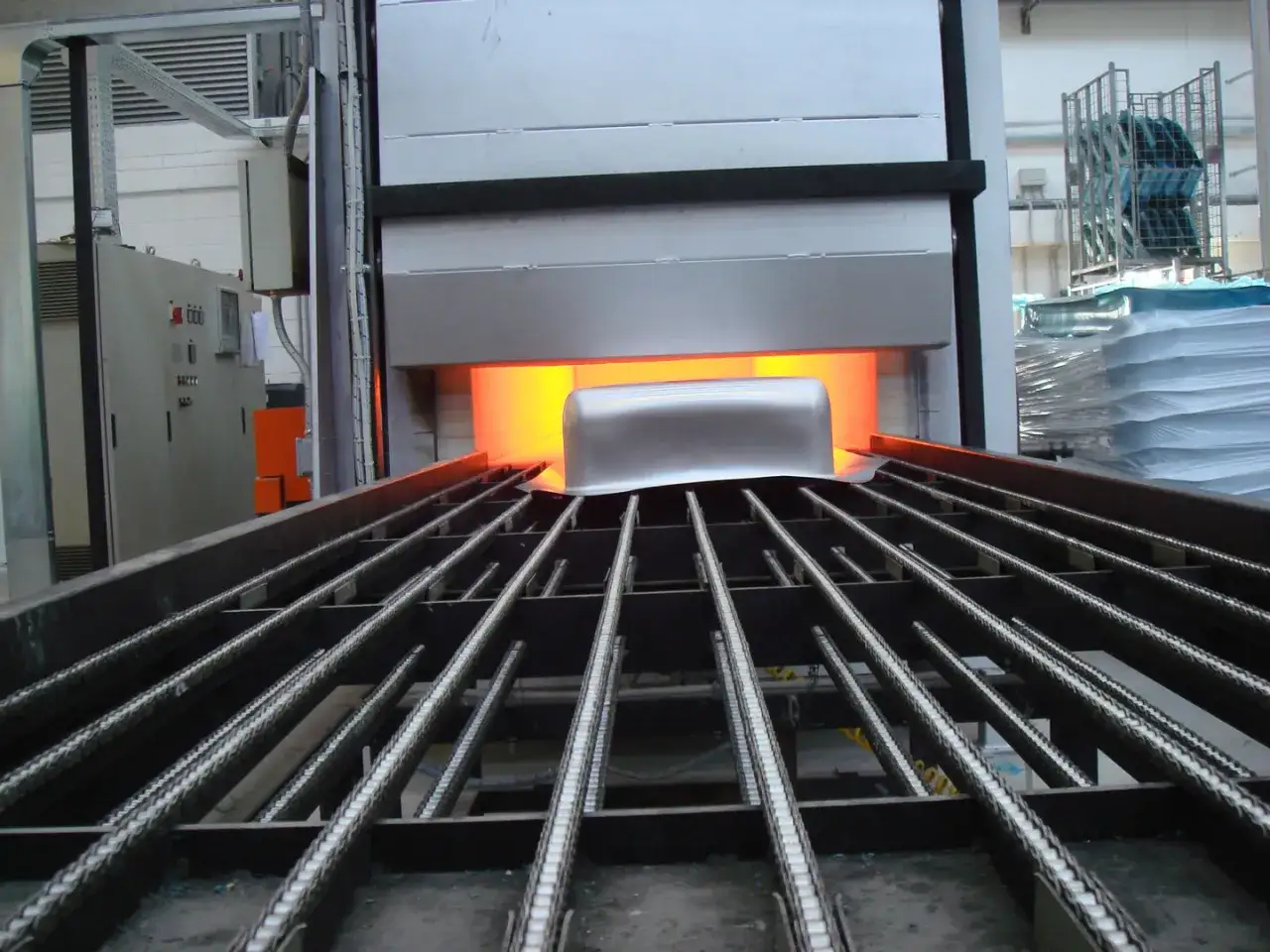 Un pezzo metallico, forse in aisi 309, entra in un forno incandescente su un nastro trasportatore.