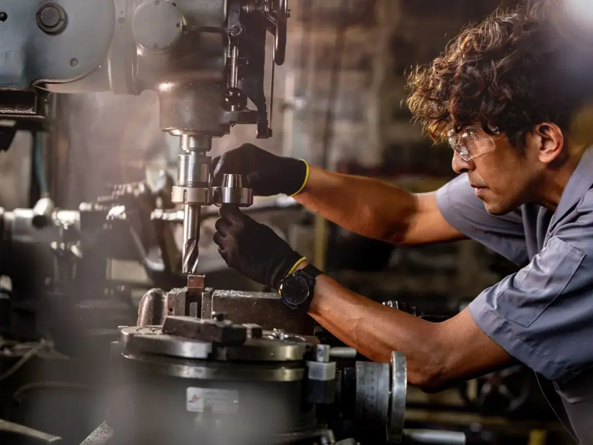 Operaio esperto esegue la manutenzione macchinari industriali, lavorando con precisione su un trapano fresatore.