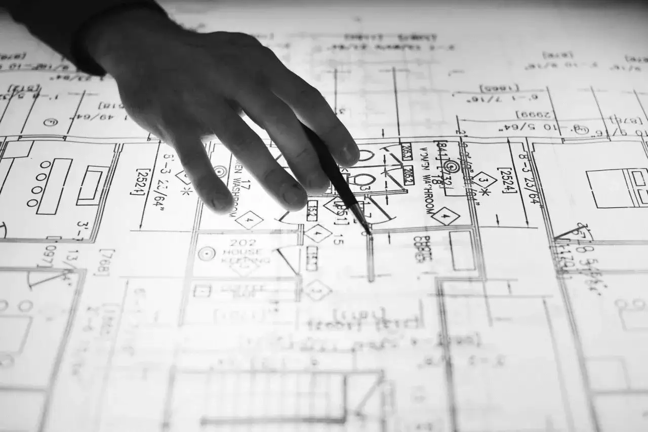 Mano di un disegnatore CAD che indica un progetto architettonico dettagliato.