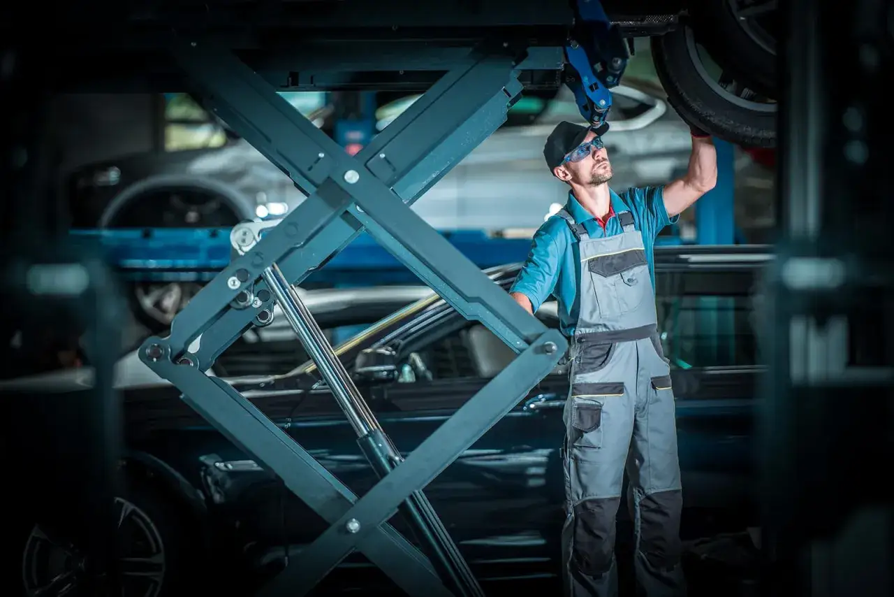 Meccanico al lavoro su un'auto sollevata, pensando a quanto guadagna un meccanico in proprio.