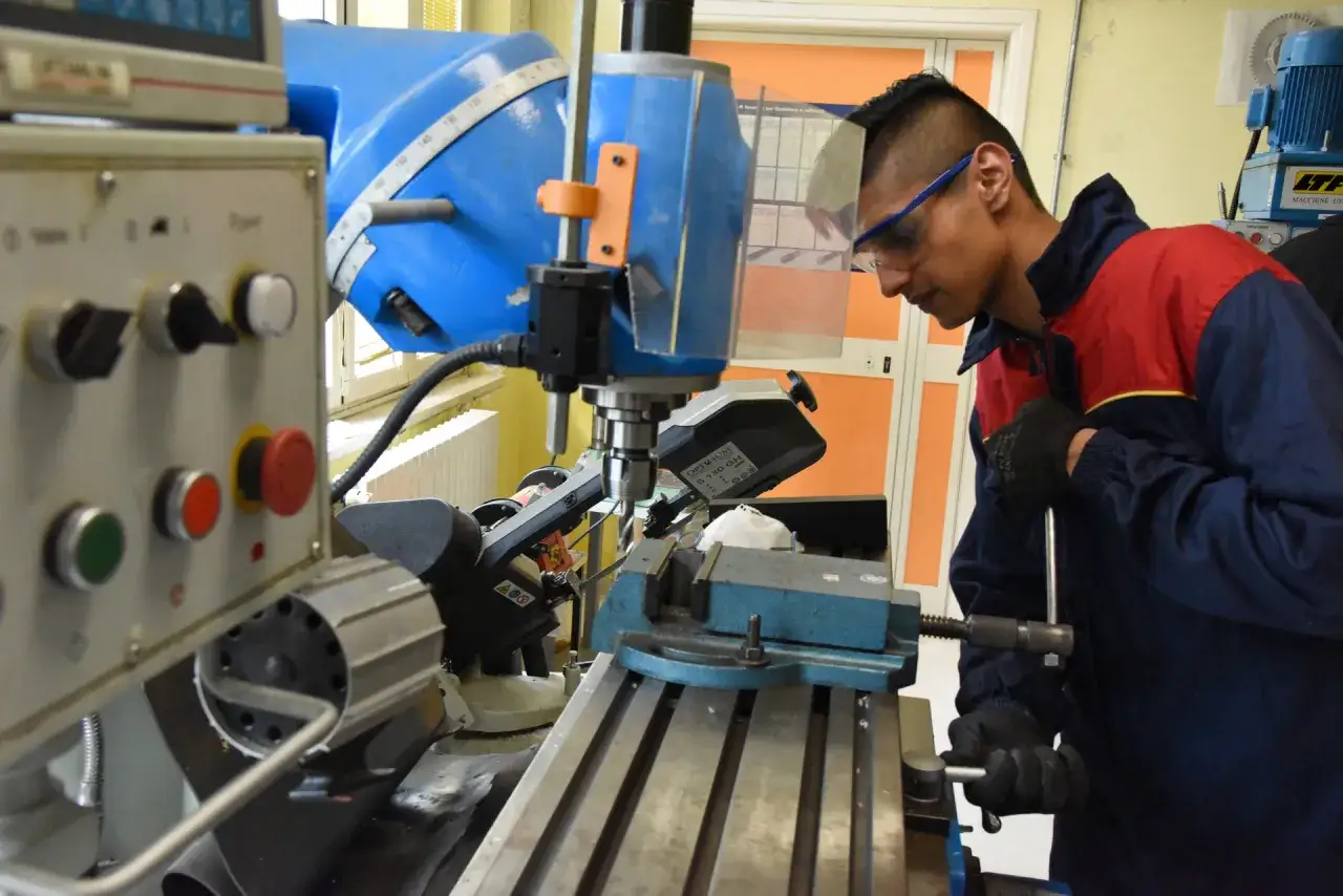 Giovane operaio con occhiali protettivi lavora con un tornitore CNC, concentrato sul pezzo da lavorare.