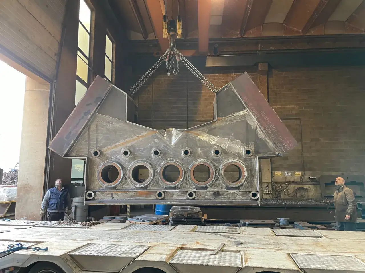 Un enorme pezzo metallico, risultato di un taglio termico, viene sollevato da un carroponte in un'officina.
