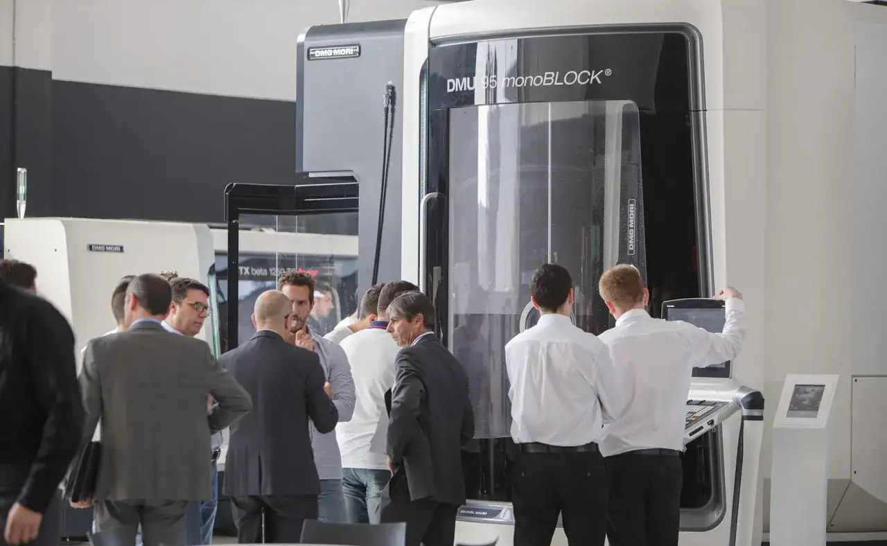 Gruppo di professionisti osserva un centro di lavoro DMG MORI 5 assi, modello DMU 95 monoBLOCK, in un ambiente industriale.