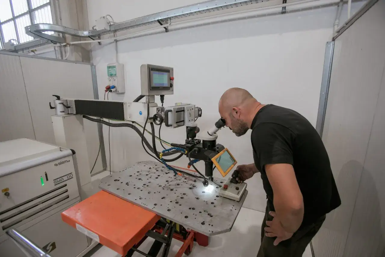 Operatore osserva con microscopio il processo di saldatura laser su un pezzo metallico.