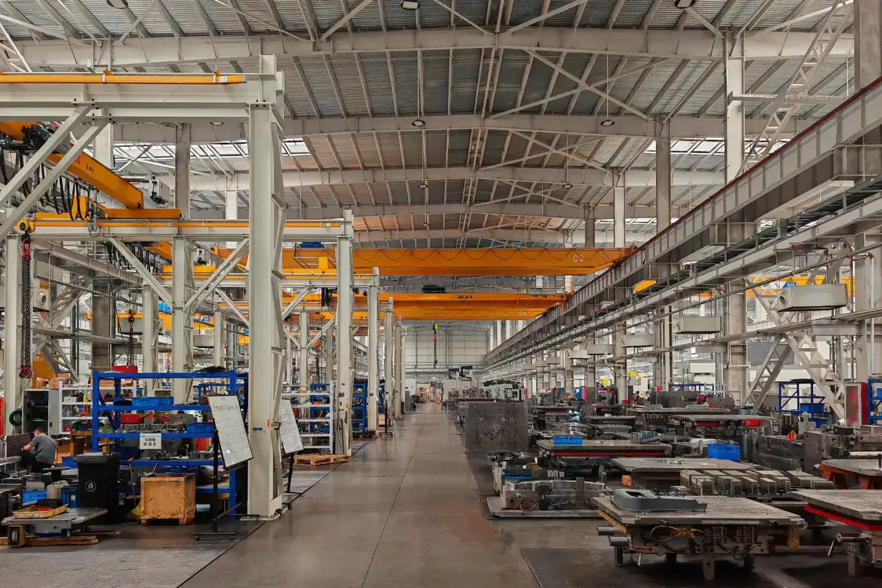 Interno di un capannone dell'industria metalmeccanica, con gru a soffitto gialle, macchinari e stampi metallici disposti in file ordinate.