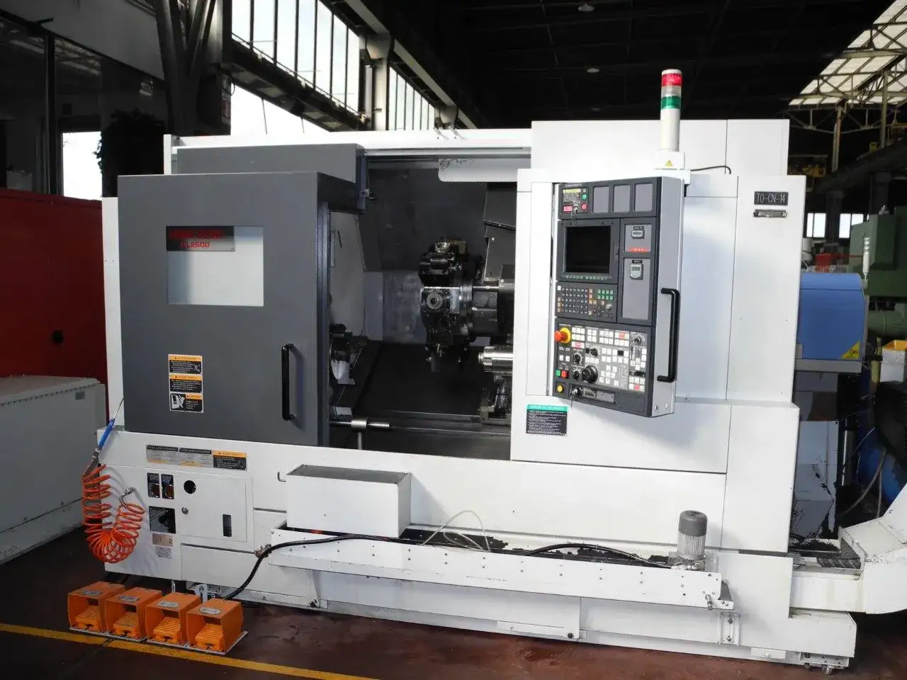 Tornio CNC Mori Seiki NL2500 in officina, con pannello di controllo e pedali pneumatici.