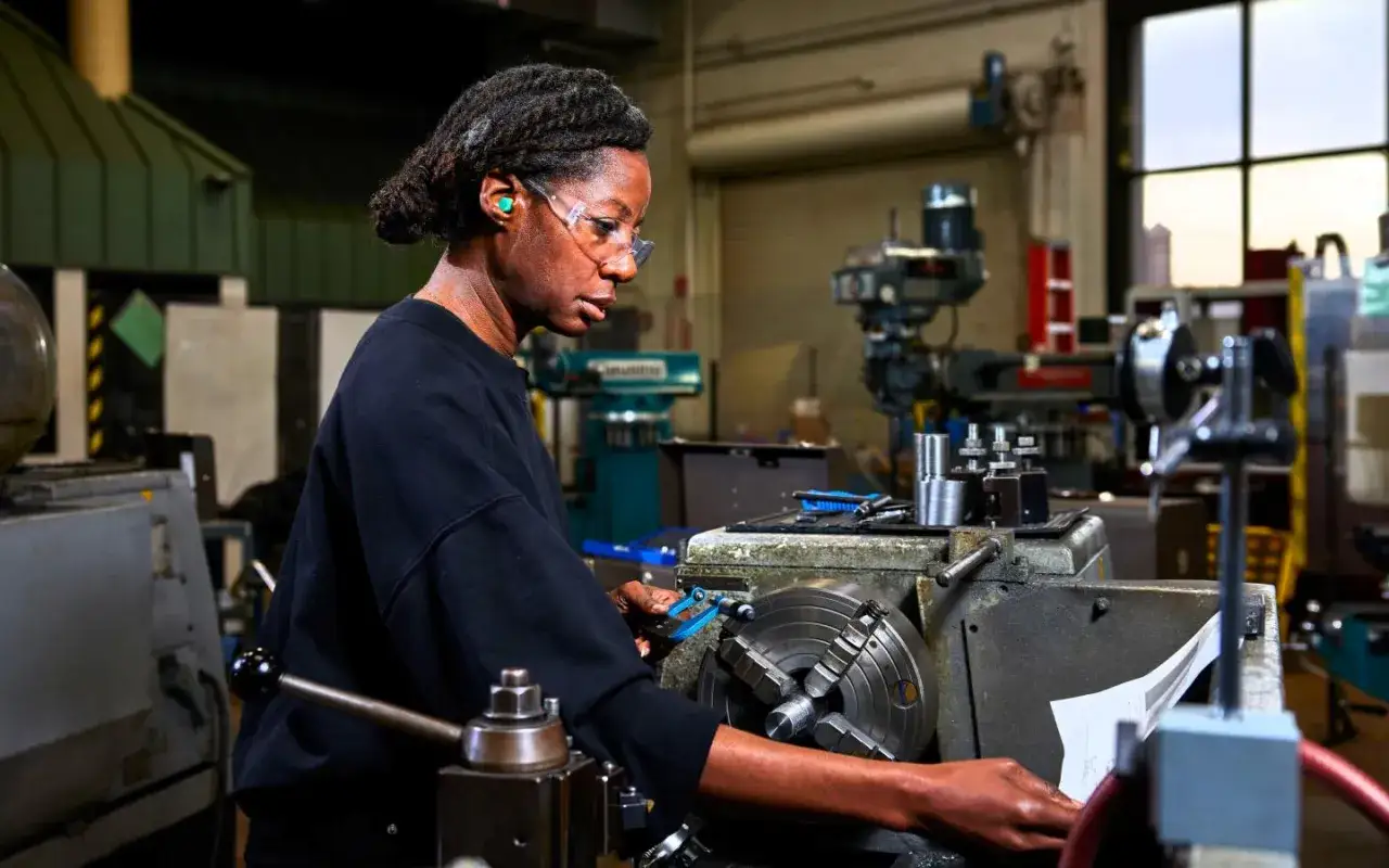 Donna lavora con macchine a controllo numerico in officina, concentrata sul progetto.