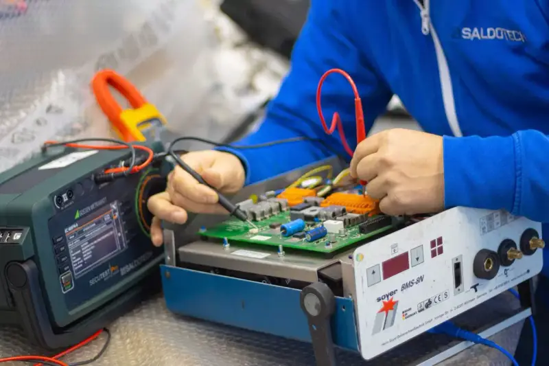 Tecnico effettua la riparazione di saldatrici, testando un circuito elettronico con strumenti di precisione.