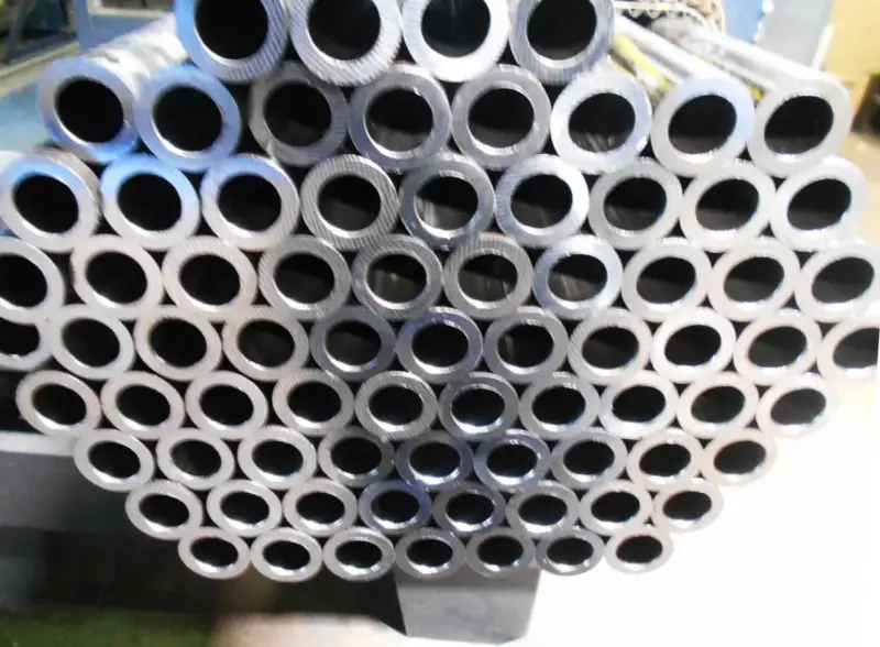 Un mucchio di tubi in acciaio al carbonio, con la sigla visibile su alcuni di essi, pronti per essere utilizzati.